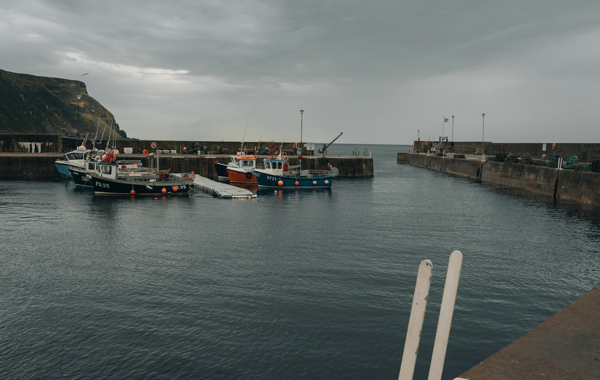 Creel boats moored inside the harbour walls under low cloud