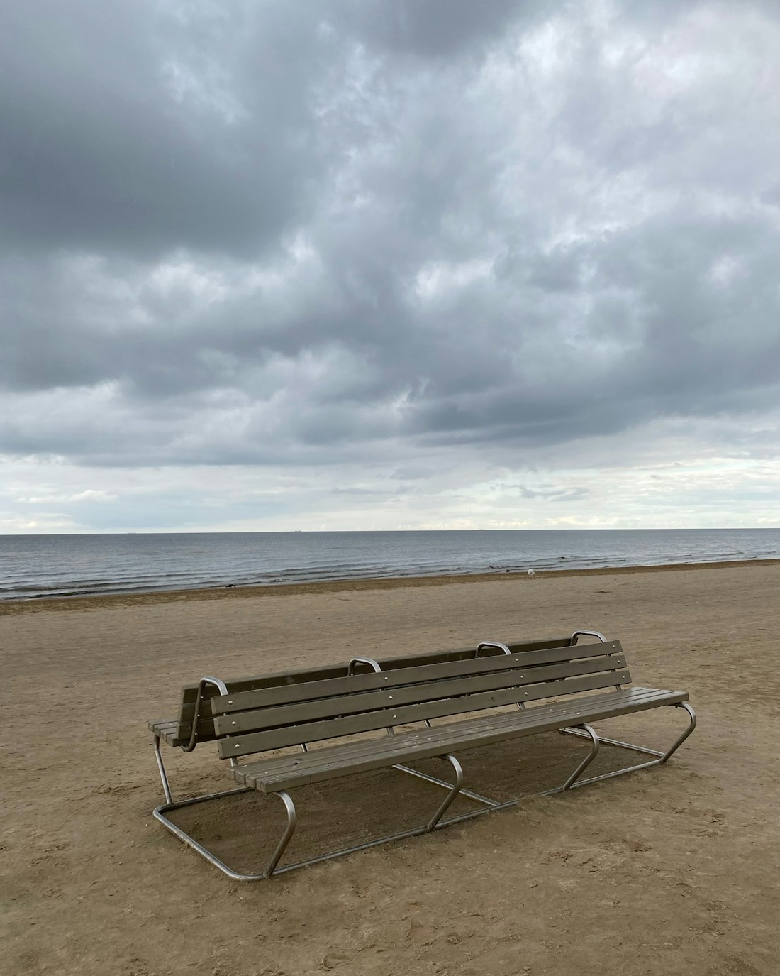 An empty bench on the sand under a heavy sky