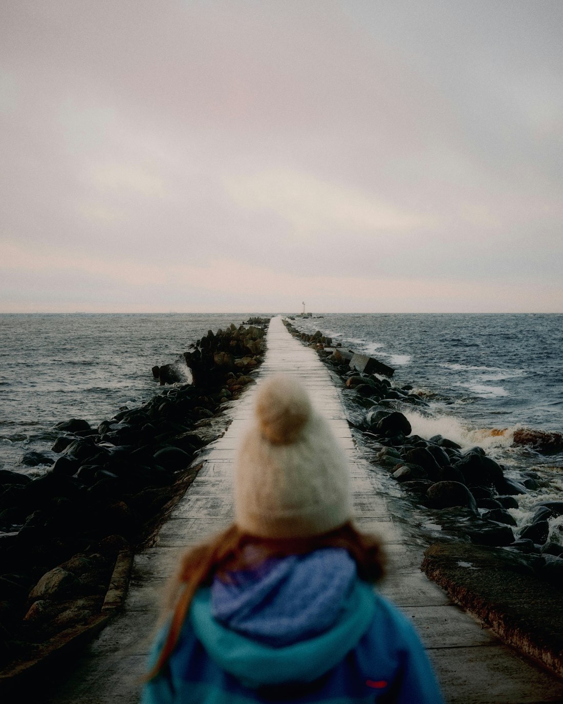 A walker in a wool hat heading out along the breakwater